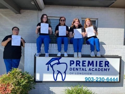 Graduates celebrating by the Premier Dental Academy sign in Longview